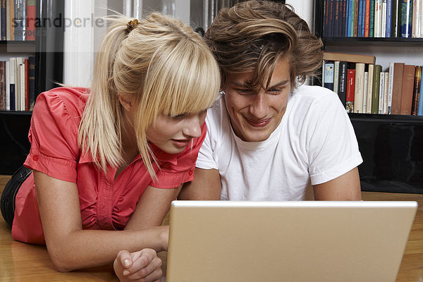 Junges Paar benutzt einen Laptop auf dem Fußboden