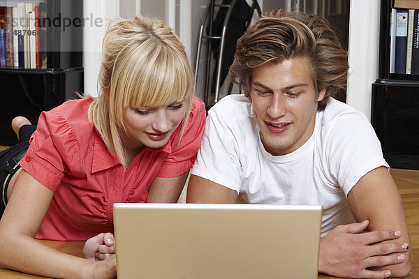 Junges Paar benutzt einen Laptop auf dem Fußboden