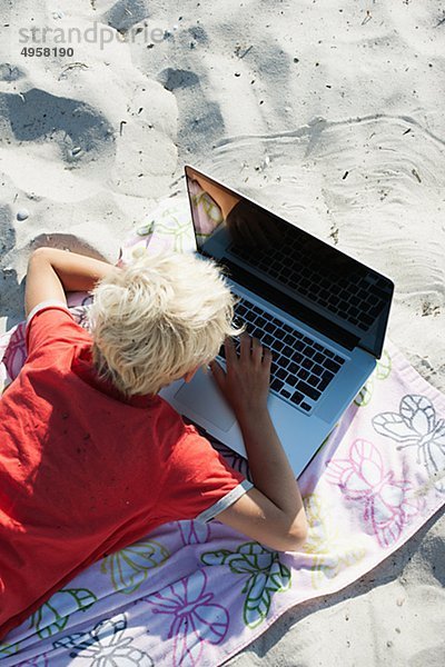 Blonde junge mit Laptop am Strand