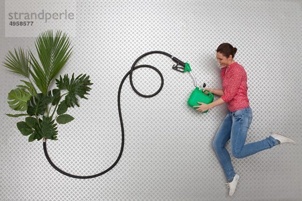 Mittlere erwachsene Frau  die Kraftstoff in Benzinkanister mit Schlauch durch Pflanzen füllt.