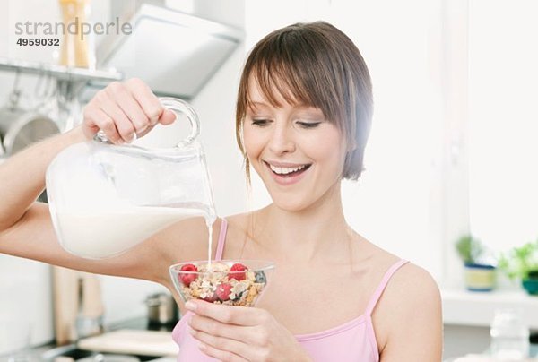 Frau gießt Milch auf Obstmüsli