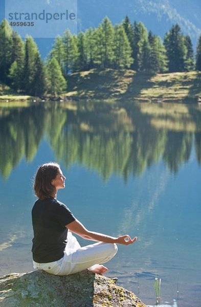 Österreich  Steiermark  Mittlere erwachsene Frau beim Meditieren am See duisitzkar in Schladming