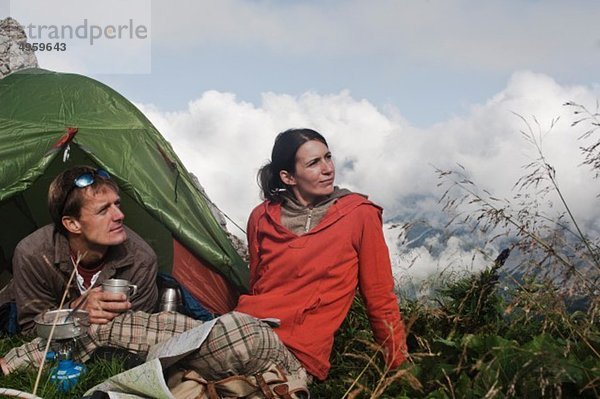 Österreich  Salzburg  Filzmoos  Paar neben Zelt auf dem Berg sitzend und mit Blick auf die Aussicht