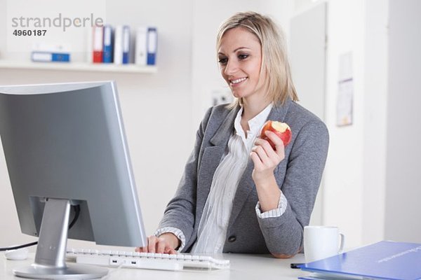 Geschäftsfrau mit Computer und Apfel in der Hand