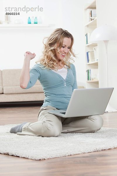 Frau auf dem Boden sitzend und mit Laptop  lachend