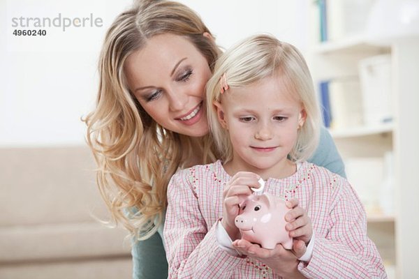 Deutschland  Bayern  München  Mutter und Tochter halten Sparschwein  lächelnd