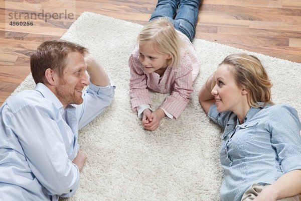 Deutschland  Bayern  München  Eltern mit Tochter auf Teppich liegend  lächelnd