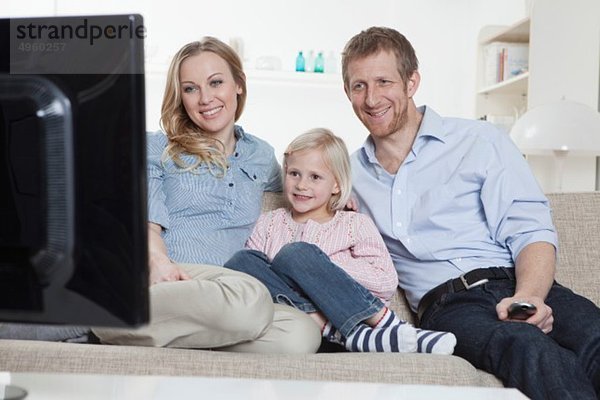 Deutschland  Bayern  München  Familie auf dem Sofa sitzend und fernsehend  lächelnd