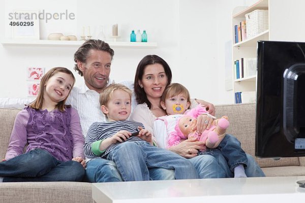 Deutschland  Bayern  München  Familie auf dem Sofa sitzend und fernsehend  lächelnd