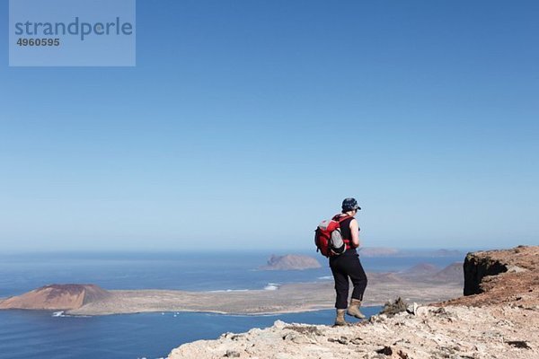 Spanien  Kanarische Inseln  Lanzarote  Risco de Famara  Reife Frau auf Klippe  Insel La Graciosa im Hintergrund
