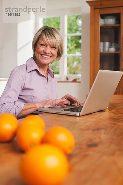 Seniorin mit Laptop und Früchten auf dem Tisch im Vordergrund