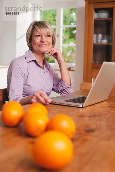 Seniorin mit Laptop und Früchten auf dem Tisch im Vordergrund