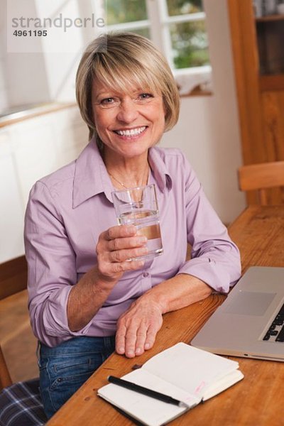 Seniorin mit Wasserglas und Laptop  lächelnd  Portrait