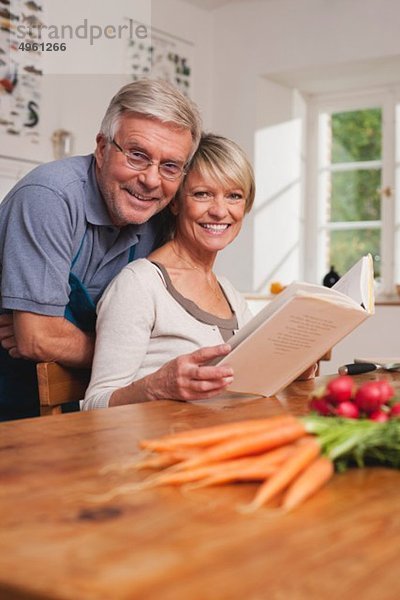 Deutschland  Kratzeburg  Seniorenpaar bei der Zubereitung von Speisen aus dem Kochbuch