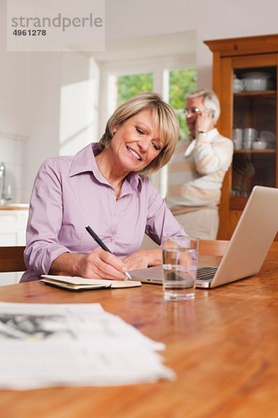 Senior Frau schreibt mit Senior Mann am Telefon im Hintergrund