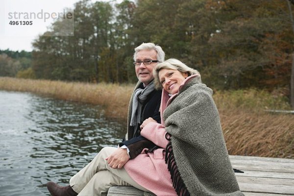 Deutschland  Kratzeburg  Seniorenpaar auf Promenade sitzend  lächelnd
