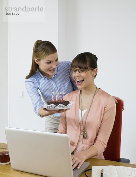 Junge Frauen mit Kuchen im Büro  lächelnd