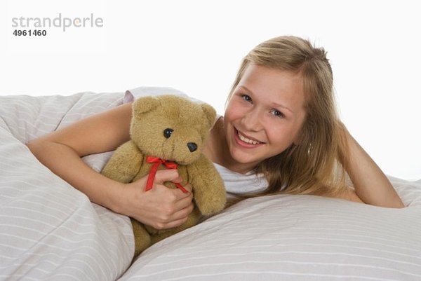 Mädchen auf dem Bett liegend mit Teddybär  lächelnd