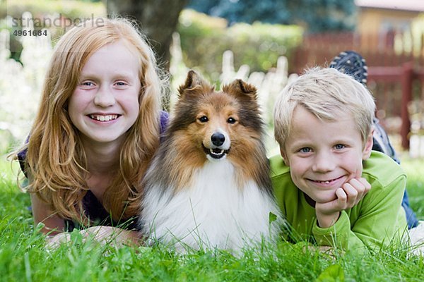 Jungen und Mädchen auf Gras liegend mit Hund