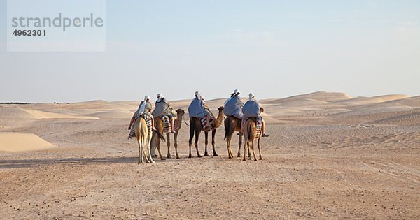 Gruppe von Menschen auf Kamelen in Wüste