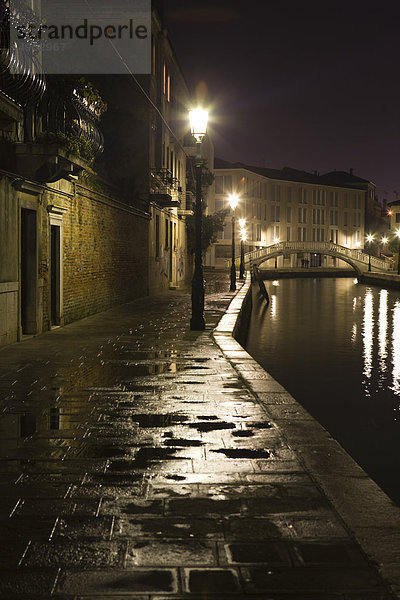 Italien  Venedig  Bürgersteig entlang des Kanals  der nachts von Straßenlaternen beleuchtet wird.
