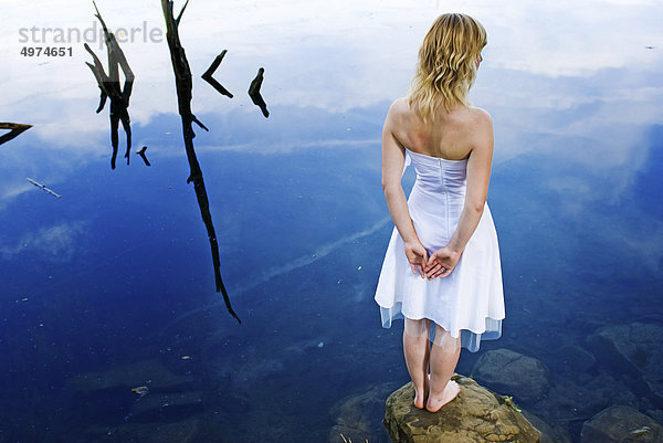 Junge blonde Frau in weißem Kleid an einem See