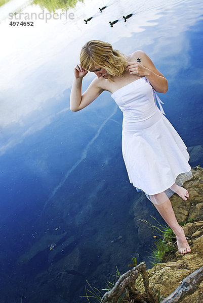 Junge blonde Frau in weißem Kleid an einem See