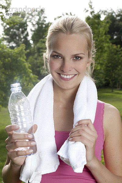 Blonde junge Frau hält eine Flasche Wasser im Freien