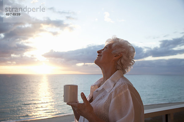 Seniorin trinkt Kaffee bei Sonnenaufgang