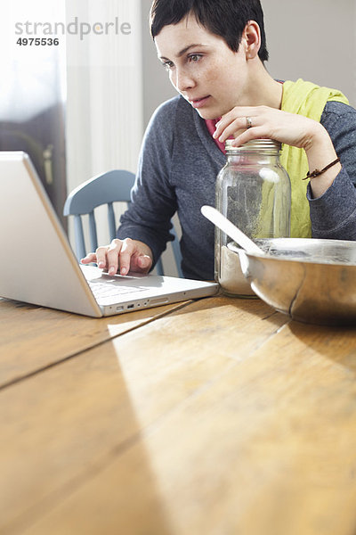 Frau schaut beim Kochen auf den Laptop