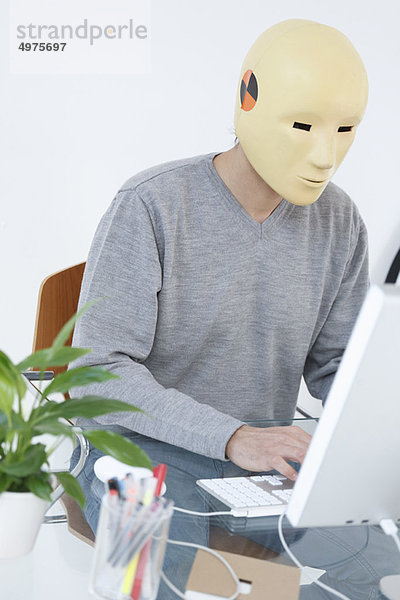 Mann in Crash-Dummy-Maske bei der Arbeit am Computer