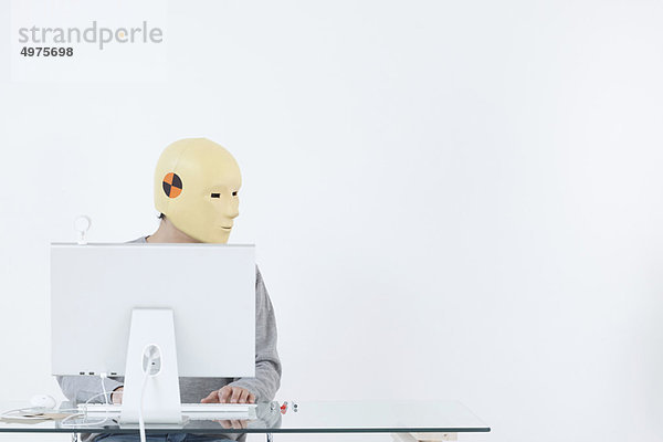 Mann in Crash-Dummy-Maske bei der Arbeit am Computer