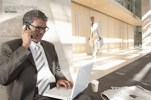 Geschäftsmann auf Laptop und Telefon