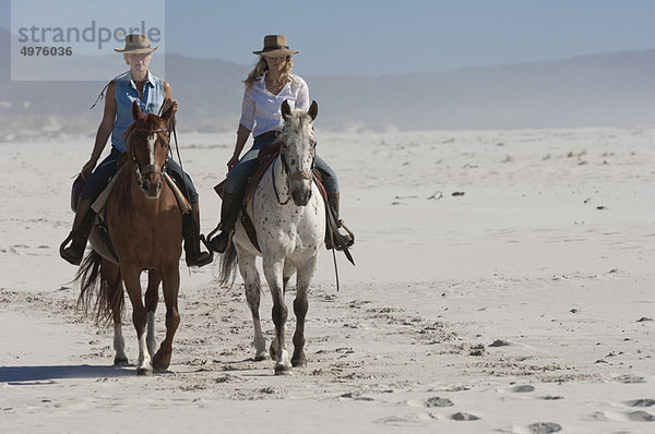 2 Personen auf Pferden am Strand