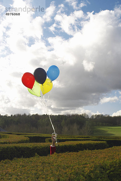 Hand hält Ballons in einem Labyrinth