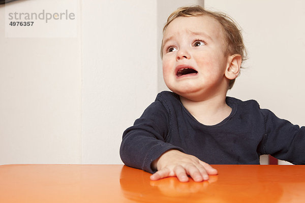 Kleiner Junge sitzt auf dem Tisch und weint.