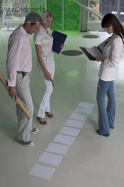 Drei Geschäftsleute schauen auf Unterlagen auf dem Fußboden