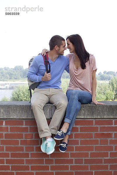 Junges Paar sitzt auf einer Mauer