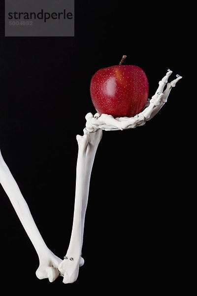 Ein Skelettarm und eine Hand  die einen roten Apfel halten.