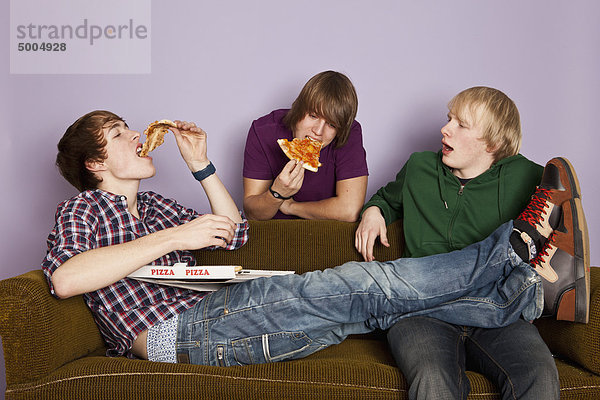 Zwei Teenager  die Pizza essen  während ein anderer neidisch zusieht.