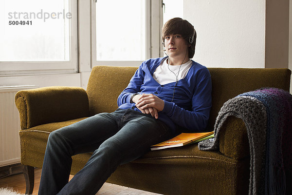 Ein Teenager  der Kopfhörer trägt und auf einer Couch sitzt.