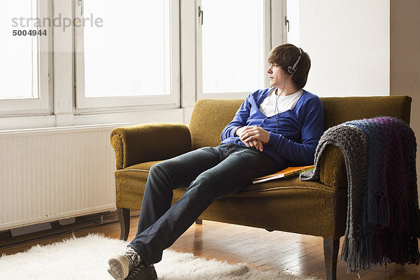 Ein Teenager  der Kopfhörer trägt und auf einer Couch sitzt.