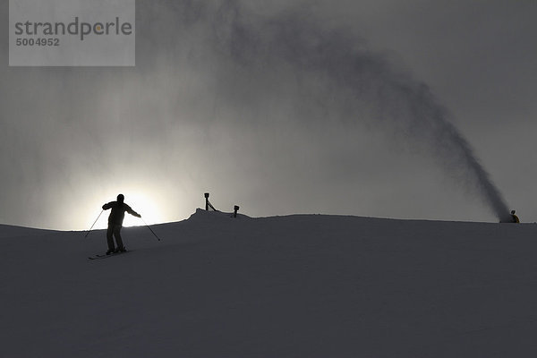 Eine Schneemaschine  die den Schnee von einem Skifahrer auf eine Piste spritzt.