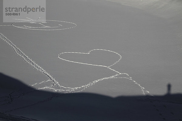 Eine Herzform und ein Smiley-Gesicht  das durch Fußabdrücke in den Schnee gestampft wurde.