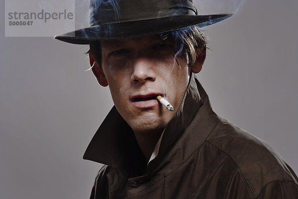 Porträt eines Mannes mit Hut und Trenchcoat beim Rauchen