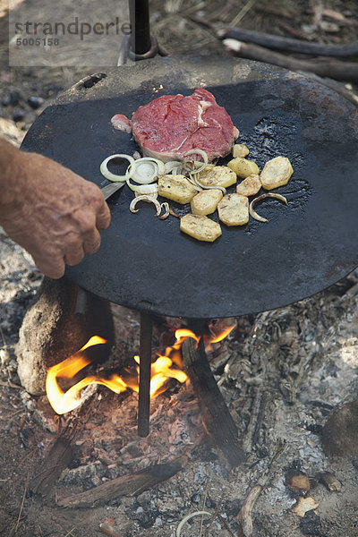 Detail eines Mannes beim Kochen am Lagerfeuer