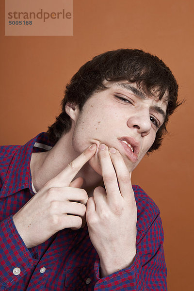 Ein Teenager knallt einen Pickel ins Gesicht  Porträt  Studioaufnahme