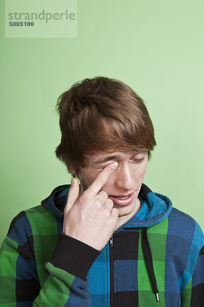 Ein Teenager reibt sich das Auge mit dem Finger  Porträt  Studioaufnahme