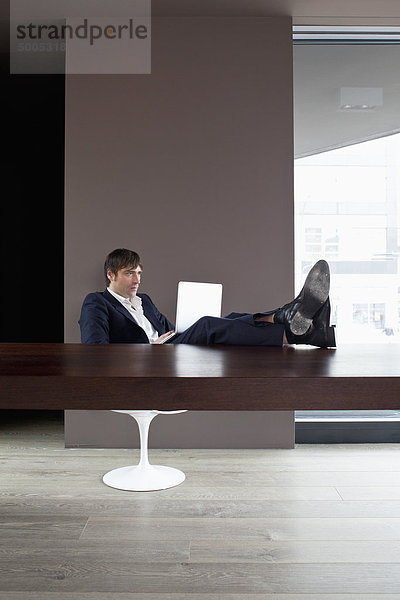 Geschäftsmann mit Füßen auf dem Tisch mit dem Laptop.