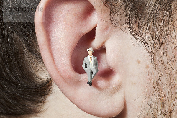 Eine Miniatur-Geschäftsmann-Figur  die im Ohr eines Mannes sitzt.